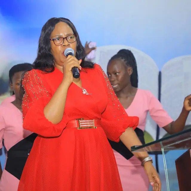 A woman in a red dress speaking into a microphone beside a lectern during a church service.
